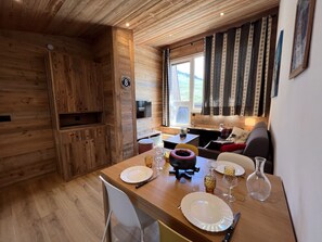A wooden interior with a dining table set for two, a sofa, and a window with curtains. - OURS BLANC 29 - Duplex with mountain views, near the aquatic center - Wi-Fi - Garage (La Clusaz)