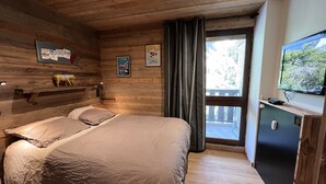 Une pièce de style cabane en bois, avec un lit, une télévision et une fenêtre avec des rideaux.