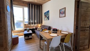 Un salon chaleureux avec un plafond en bois, un canapé, une table à manger avec des chaises et une fenêtre avec des rideaux.