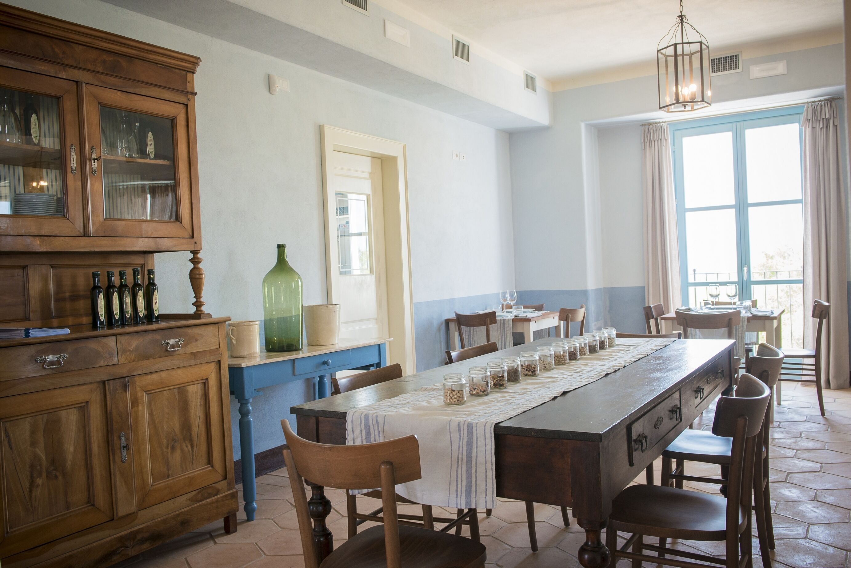 Un comedor con una larga mesa de madera, sillas y un mueble de madera con puertas de cristal.