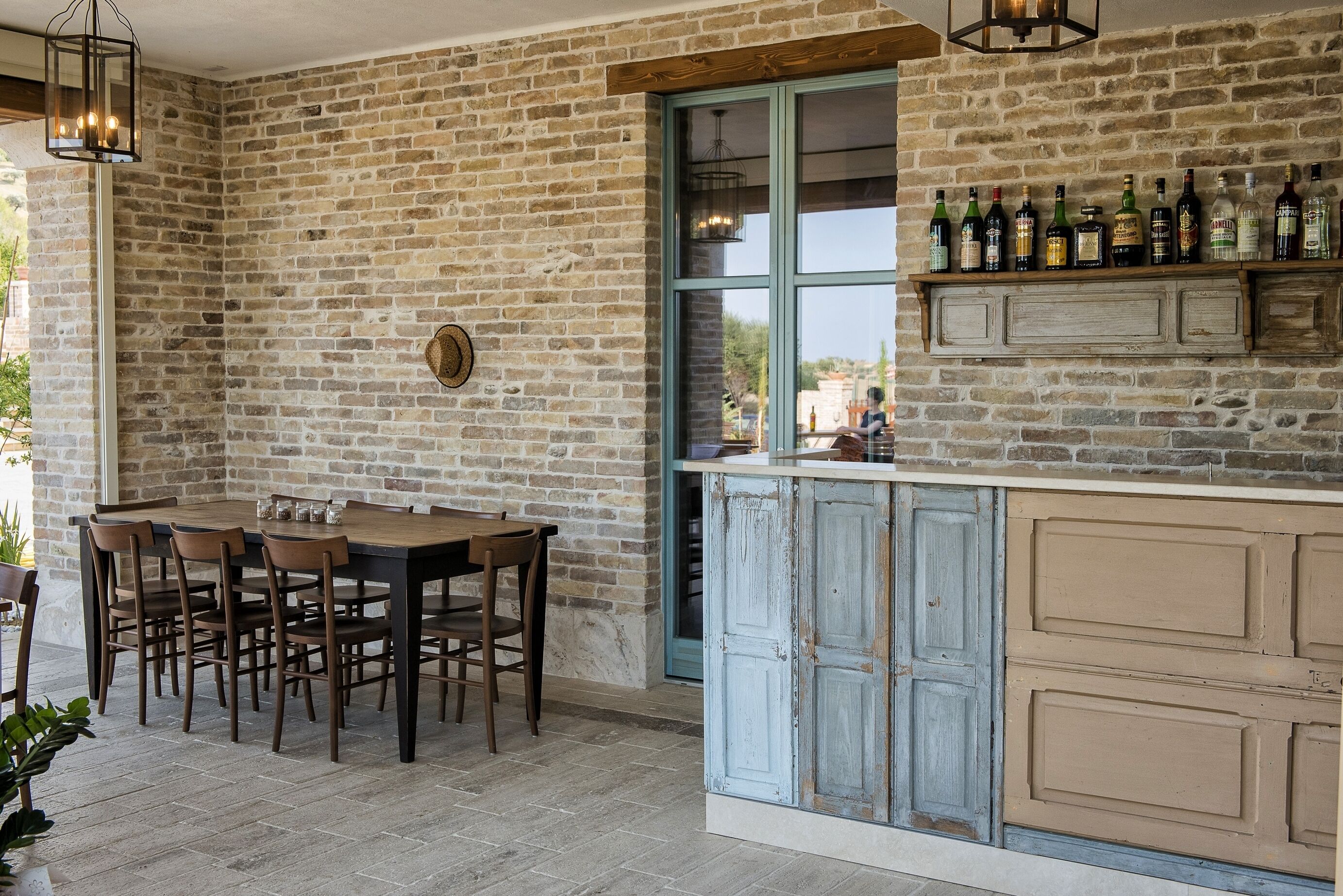 Een rustieke keuken met een bakstenen muur, een houten eettafel met stoelen en een wijnrek met flessen.
