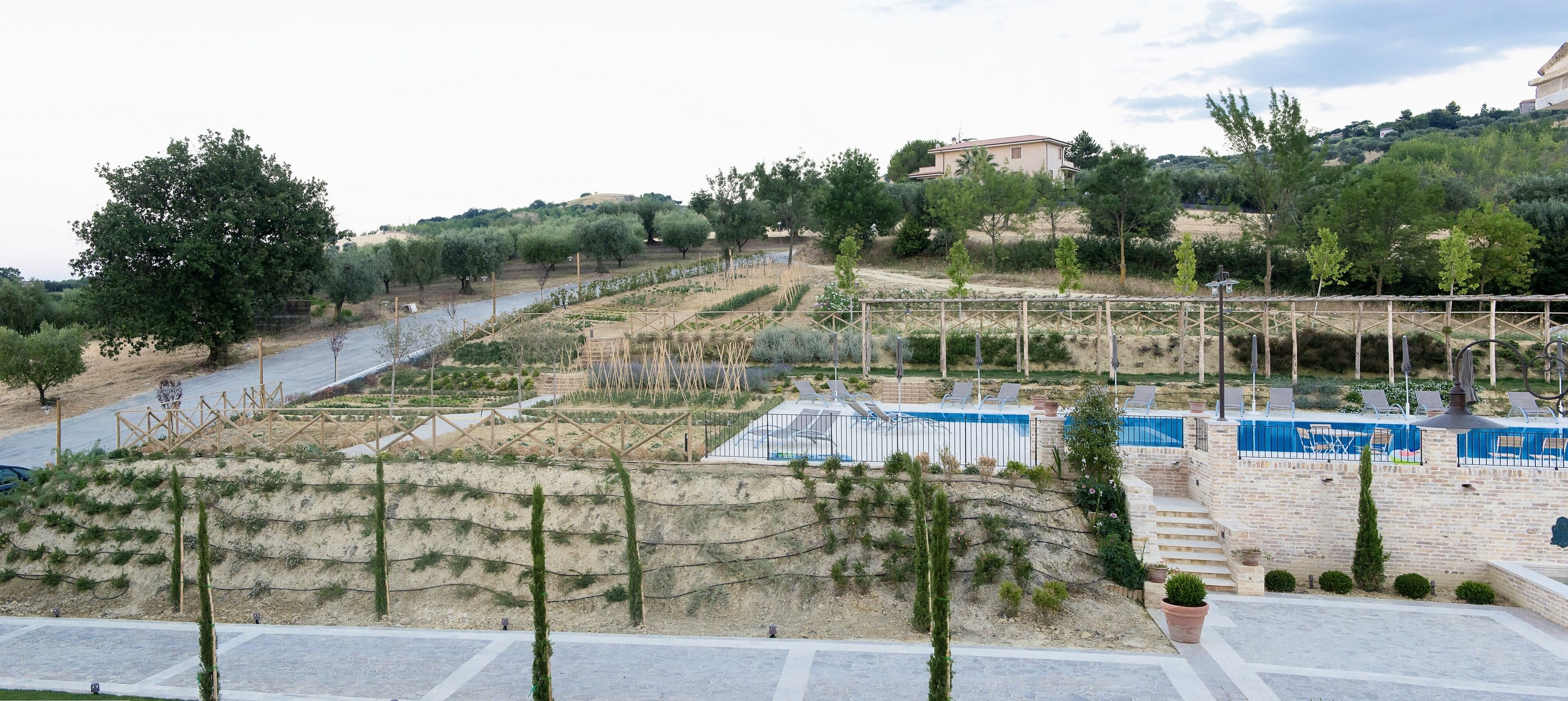 A landscaped area with a swimming pool, steps leading to a poolside area, and a view of a hillside with trees and a building in the distance.