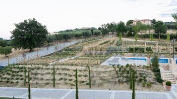 A landscaped area with a swimming pool, steps leading to a poolside area, and a view of a hillside with trees and a building in the distance.
