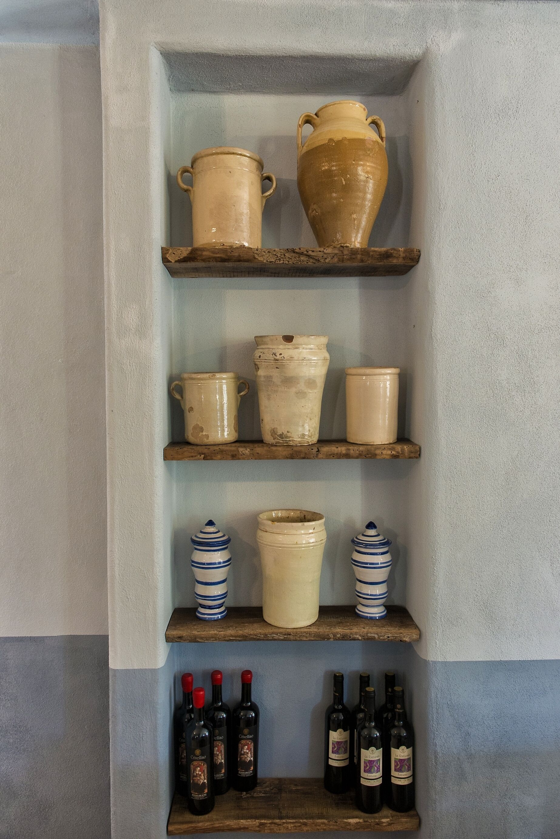 A shelf with various ceramic containers and wine bottles.