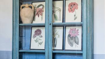 A teal cabinet with glass doors, displaying various ceramic items and framed botanical illustrations.
