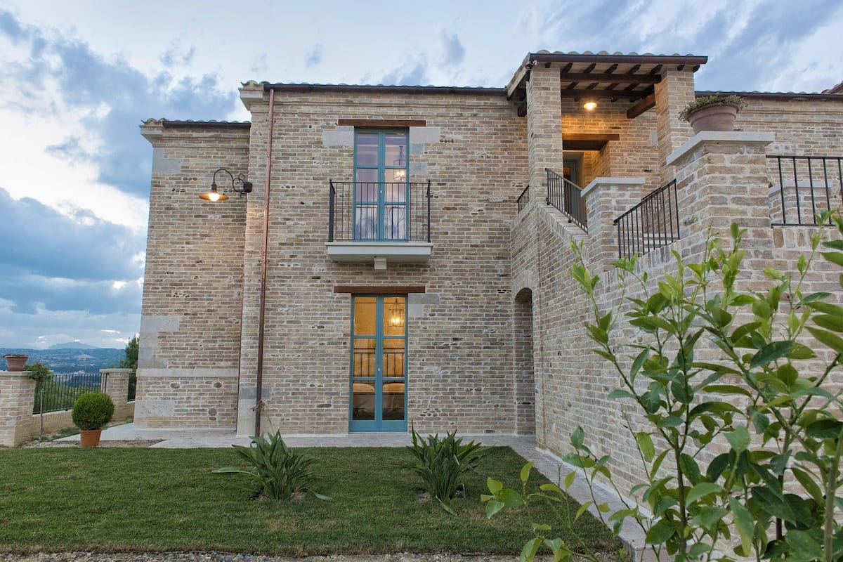 A stone building with a central entrance, a balcony, and a small garden area.