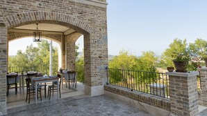 A stone patio with tables and chairs, a hanging light fixture, and a view of trees and hills. - Villa Sant'Angelo (Alba Adriatica)