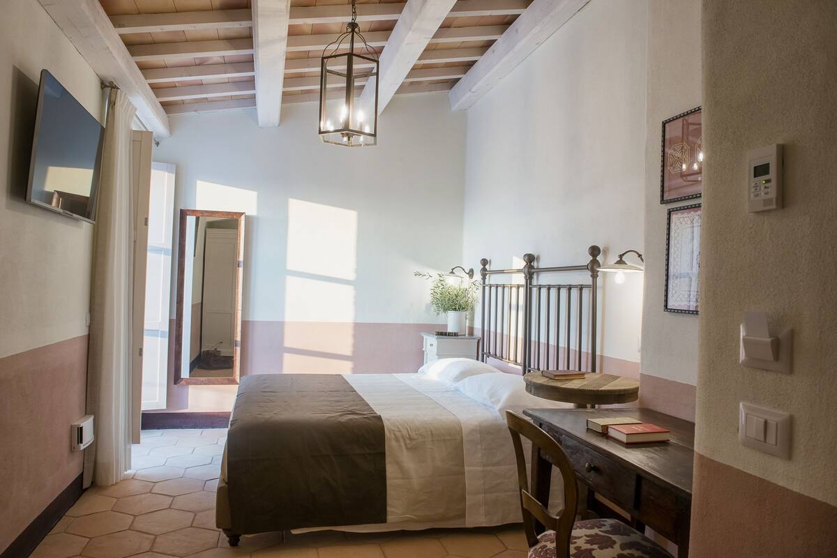 A bedroom with a bed, a desk, a chair, a potted plant, and a window.