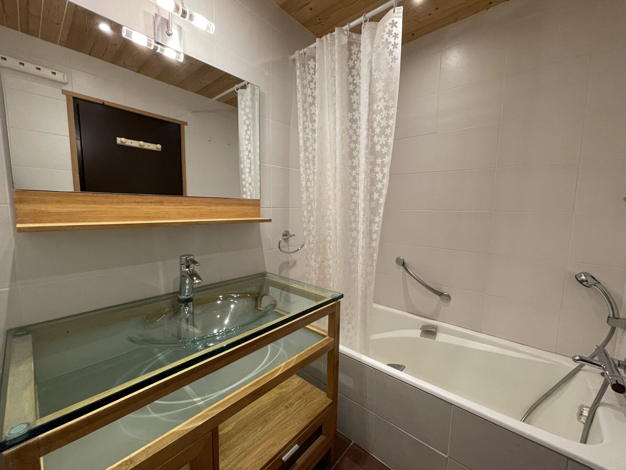 Ein modernes Badezimmer mit einem Glaswaschbecken, einem Holzausziehtisch, einem großen Spiegel, einer Badewanne und einer Dusche mit Vorhang.