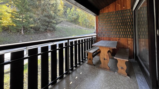 A wooden deck with a bench and a view of a forested hillside. - BELMONT 26 – Village-center duplex close to the slopes (La Clusaz)