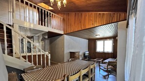 A spacious room with a wooden staircase, a dining area with a table and chairs, and a cozy seating area with a sofa and a television. - BELMONT 26 – Village-center duplex close to the slopes (La Clusaz)