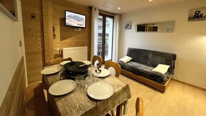 A cozy wooden interior with a dining table set for two, a sofa, and a TV mounted on the wall. - GENTIANES 3 – Apartment in the village center and close to ski slopes – Wi-Fi (La Clusaz)