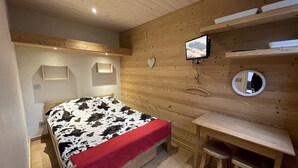 A wooden-paneled bedroom with a bed, a desk, and a mirror. - GENTIANES 3 – Apartment in the village center and close to ski slopes – Wi-Fi (La Clusaz)