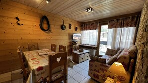 Een knus houten interieur met een eettafel, stoelen, een bank en een televisie.