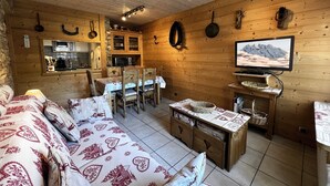 Een gezellig houten hutje van binnen met een eethoek, keuken en een televisie waarop een uitzicht op de bergen te zien is.