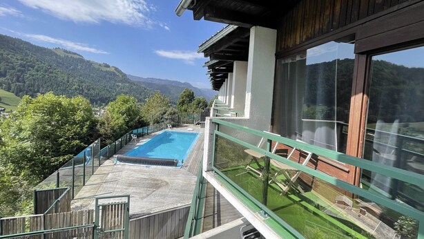 A modern building with a pool, wooden deck, and a view of mountains.