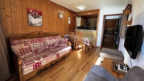 A cozy cabin interior with a wooden sofa, a dining table, and a kitchen area.