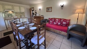 A dining area with a wooden table set for six, a red sofa, and a grey armchair. - PETIT LUTIN – Chalet on the slopes and in the village center – Garage and parking (La Clusaz)