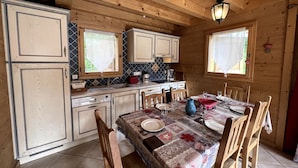 Ein Interieur einer Holzhütte mit einem Esstisch, gedeckt für vier Personen, Holzausbau, einer gefliesten Spritzschutzwand und einer Pendelleuchte.