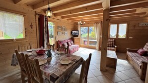 Ein Holzblockhaus-Interieur mit einem Esstisch für vier Personen, einer Couch und einem Fernseher.