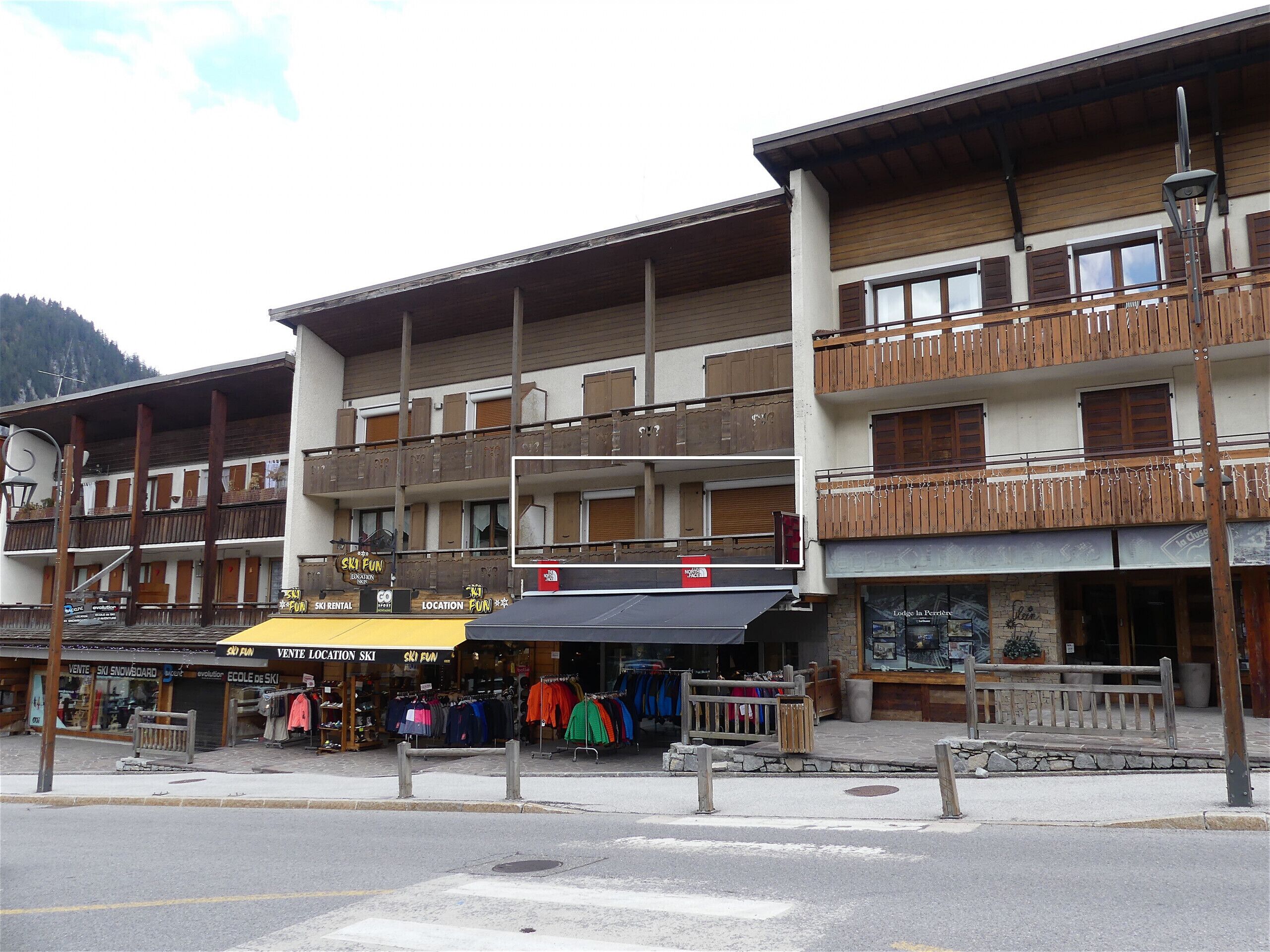 Un immeuble à plusieurs étages doté de balcons, d’un magasin de location de matériel de ski et de divers commerces au rez-de-chaussée.
