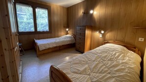 Una stanza con due letti di legno, una cassettiera e una finestra vista alberi.