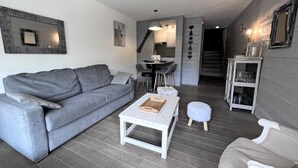 Ein modernes Wohnzimmer mit einem grauen Sofa, einem weißen Couchtisch und einem Essbereich mit einem kleinen Tisch und Stühlen.