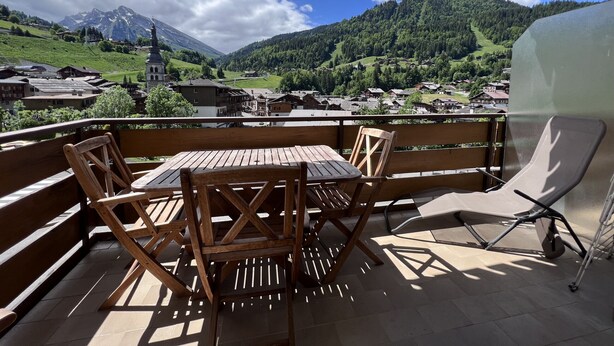 Ein Holztisch und -stühle auf einem Balkon mit Blick auf ein Dorf und Berge.