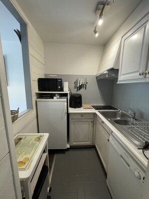 A compact kitchen with a microwave, coffee maker, and knife set on the wall, a refrigerator, a sink, and a window with a view.