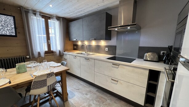 Une cuisine moderne avec un plafond en bois, une cuisinière encastrée et un coin repas avec une table dressée pour quatre personnes.