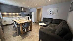 Une cuisine moderne avec un coin repas, un canapé en cuir noir et un tableau représentant un chien blanc accroché au mur.