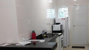 A kitchen with a white tiled backsplash, a black countertop, and two black bar stools. There is a window with a view of trees, a white refrigerator, and a microwave. - Casa no Mirante de Escarpas (Capitólio)