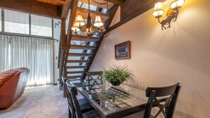 Un coin repas avec une table à plateau en verre, des chaises noires, une plante en pot et un escalier avec des rampes en bois.