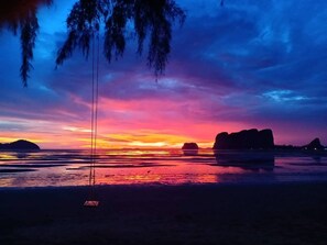 A beach scene with a swing, calm water, and distant rock formations during sunset. - Blue Lagoon Home Trang (Kantang)