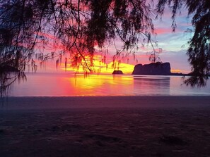A sunset over a calm lake with silhouettes of rocks and trees. - Blue Lagoon Home Trang (Kantang)