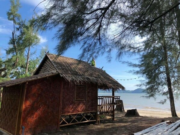 A rustic hut with a thatched roof, situated on a sandy beach with a view of the sea and mountains in the distance. - Blue Lagoon Home Trang (Kantang)