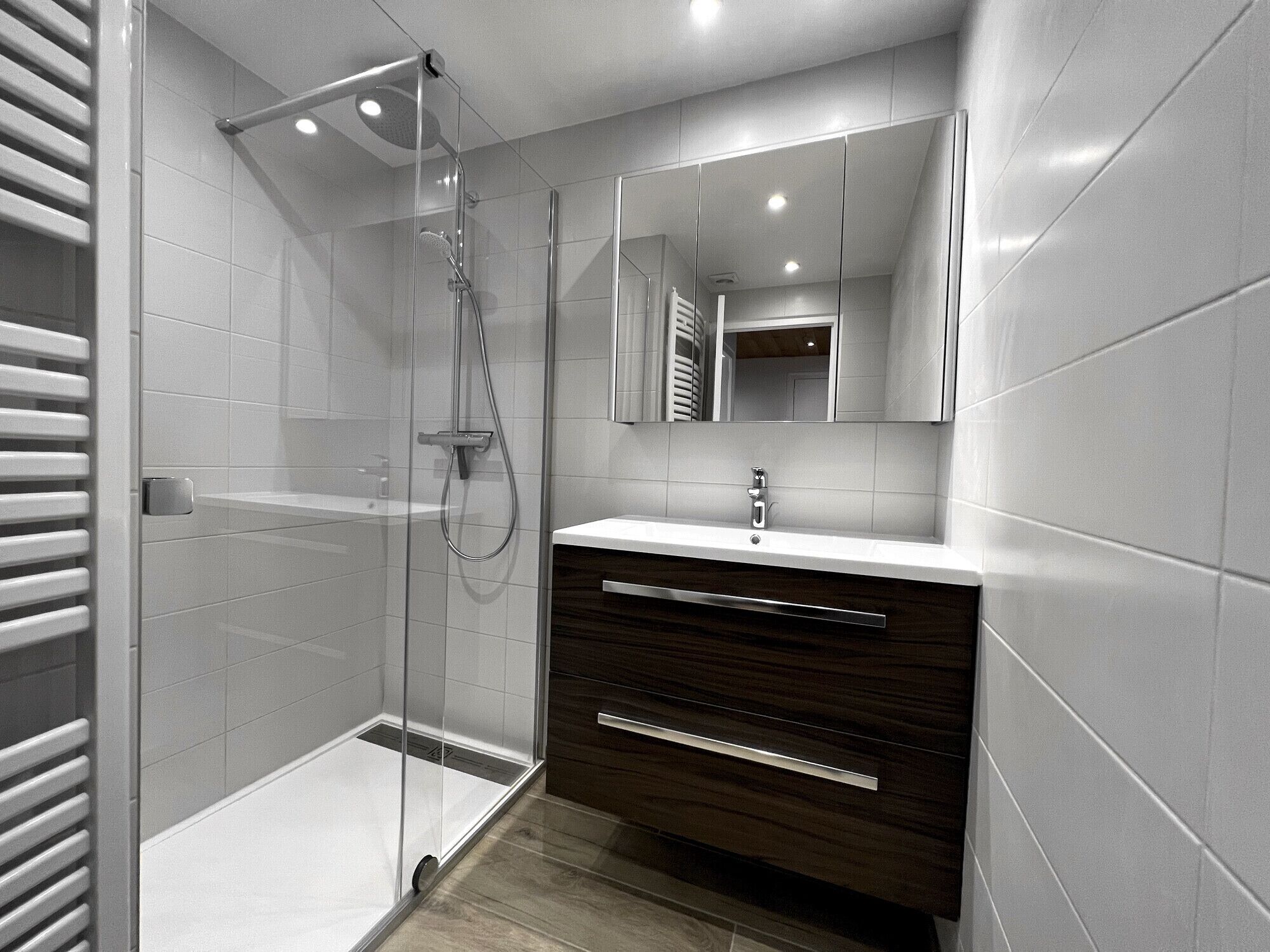 A modern bathroom with a glass-enclosed shower, a wooden vanity, and a large mirror.