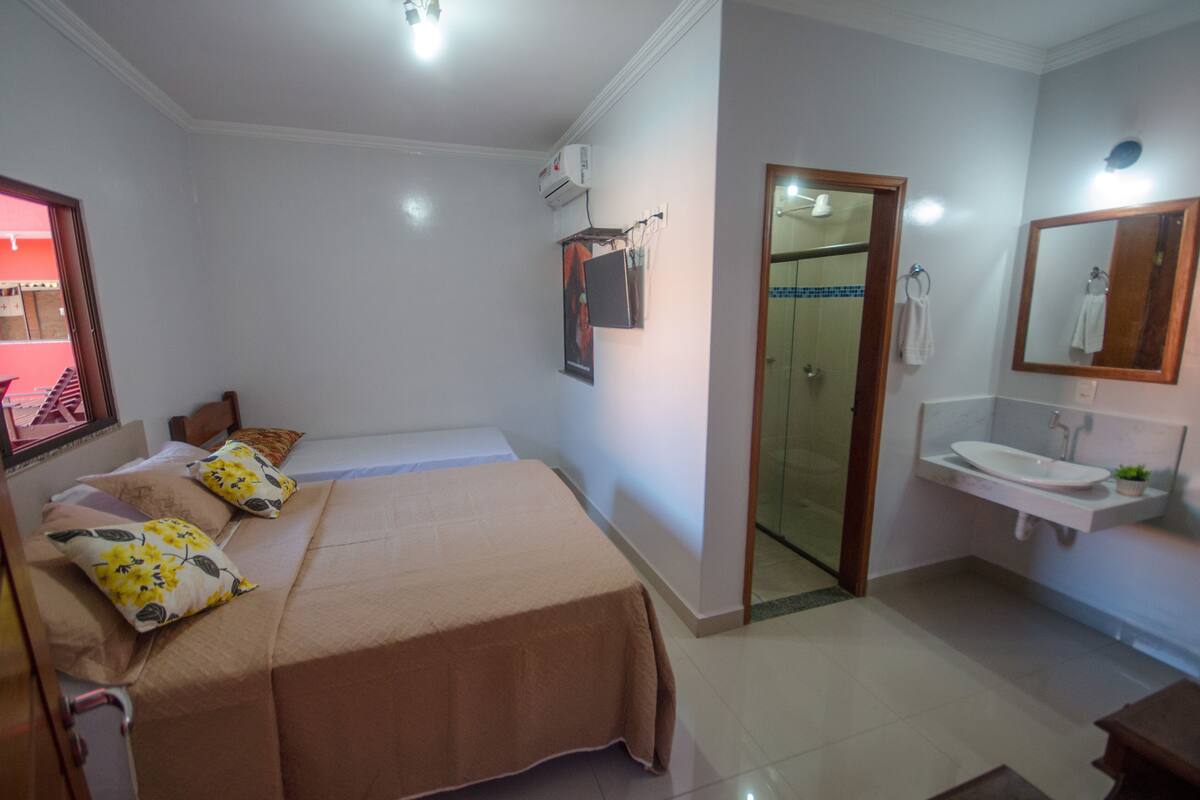 A hotel room with a bed, a bedside table, a mirror, a sink, and a shower area.