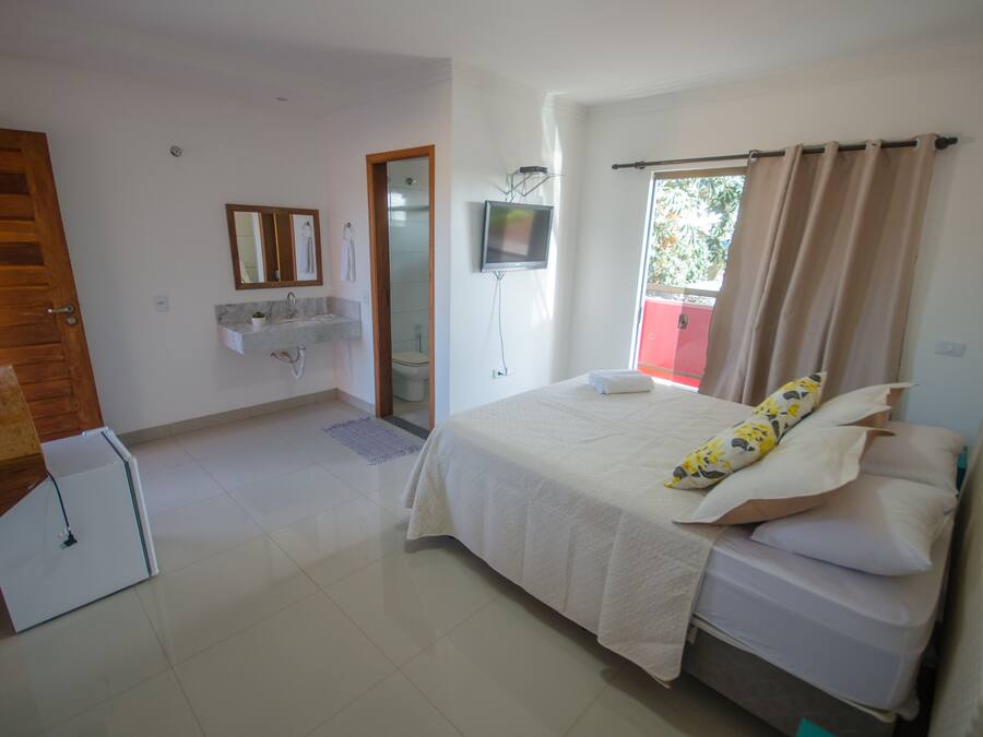 A bedroom with a bed, a TV, a bathroom with a sink, and a door.