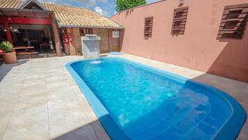 A swimming pool with a tiled deck, a brick wall, and a building with a red facade and a tiled roof.