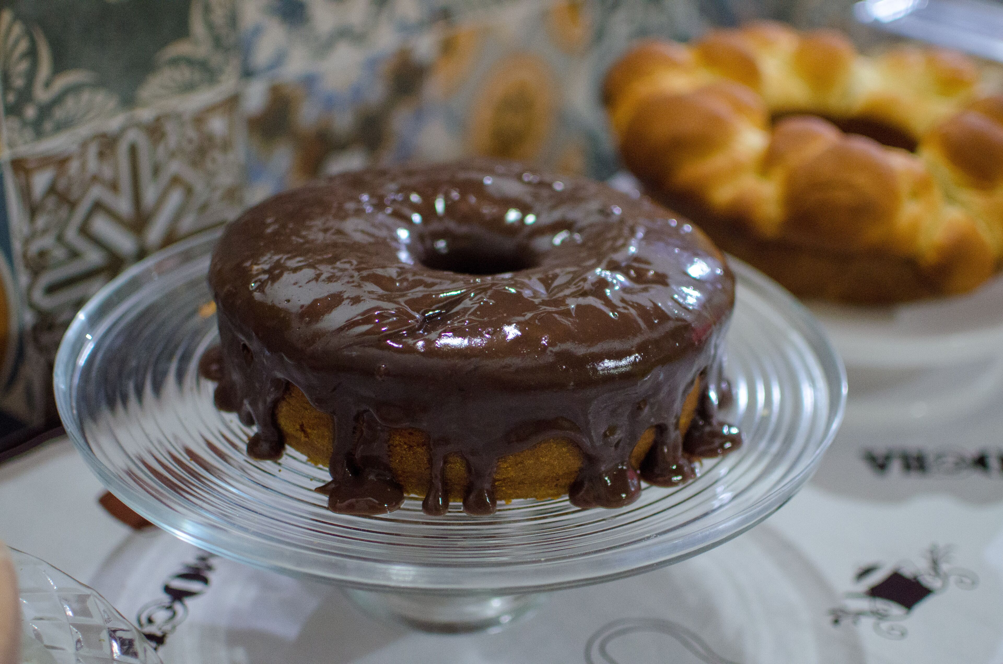 Un dolce tipo donut glassato al cioccolato su un piatto di vetro trasparente.