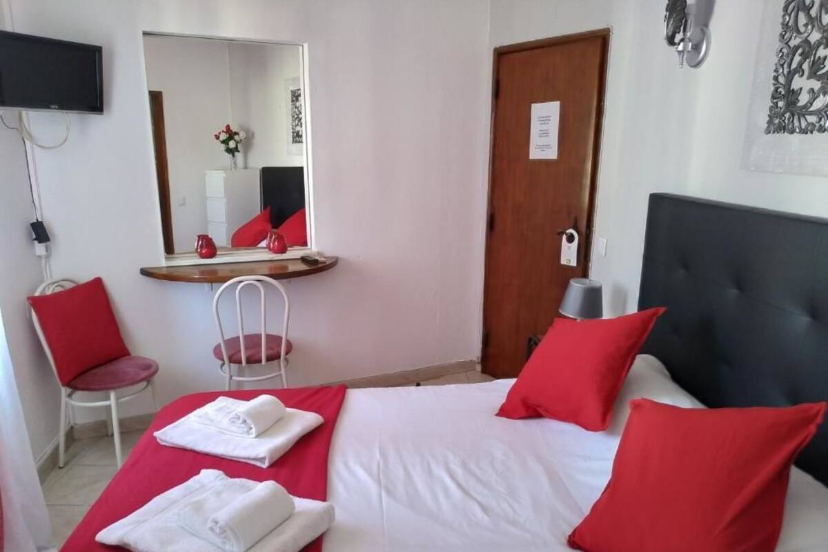 Ein Hotelzimmer mit einem Bett, einem Sessel, einem Schreibtisch, einem Spiegel und einer Tür.