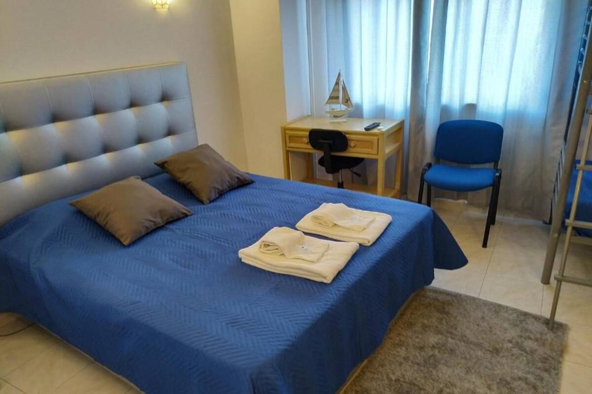 Ein ordentlich gemachtes Bett mit blauer Bettdecke, zwei Kissen und gefalteten Handtüchern auf einem Nachttisch daneben.