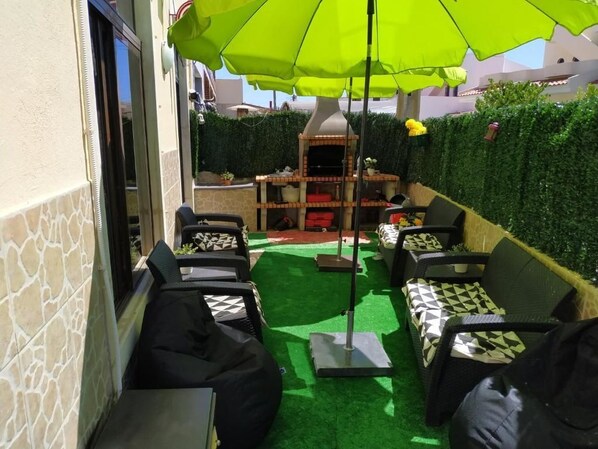 An outdoor patio with a barbecue grill, green artificial turf, and black and white patterned outdoor furniture.