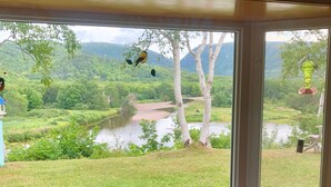 Ein Zimmer mit einem großen Fenster mit Blick auf eine üppige Landschaft, inklusive Fluss, Bäume und Hügel.