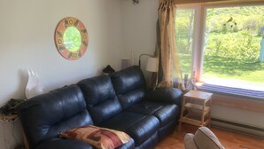 Ein Wohnzimmer mit einer schwarzen Ledersofa, einem Holztisch und Blick auf eine grüne Landschaft durch ein Fenster.