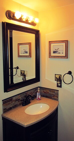 A bathroom with a large mirror, a sink, and framed pictures on the wall.