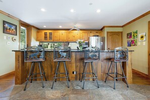 A kitchen with wooden cabinets, a central island with bar stools, a ceiling fan, and artwork on the walls. - 3 BR/3BA Platinum Vail /Lionshead Penthouse
4 min walk to Lionshead gondola! (Vail)