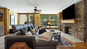 Una sala de estar amplia con chimenea de piedra, un televisor de pantalla plana grande y un área de descanso confortable con sofá y sillones.