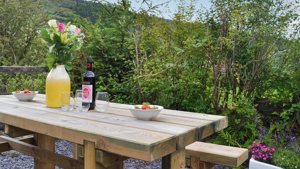 A wooden picnic table with a bottle of wine, a glass, and bowls of strawberries and flowers. - 2 bedroom accommodation in Penmachno, near Betws-Y-Coed (Penmachno, near Betws-Y-Coed)